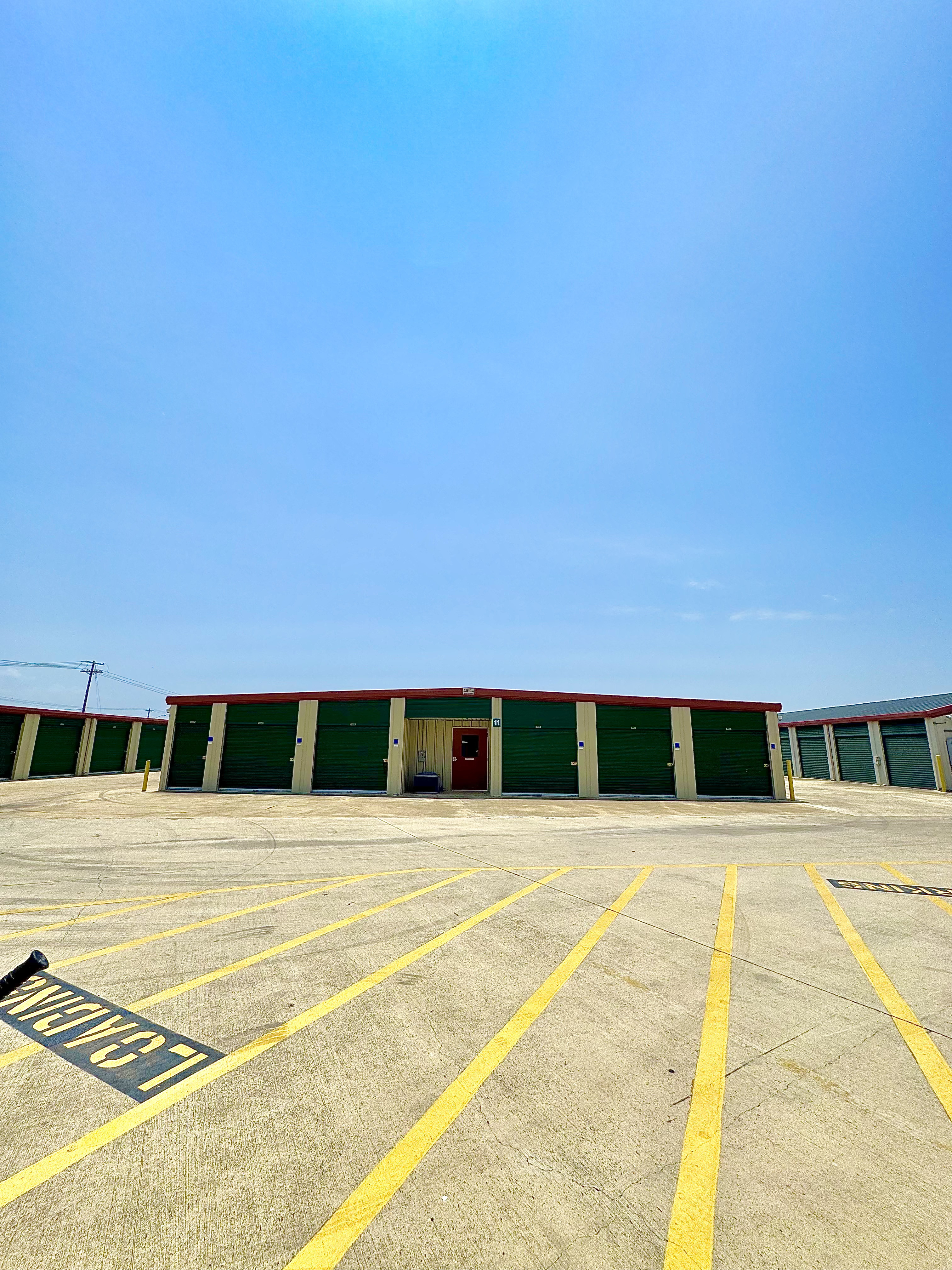 Exterior view of LockSmart Climate Storage facility with green roll-up doors, climate-controlled units, and designated loading zone in Lockhart, TX